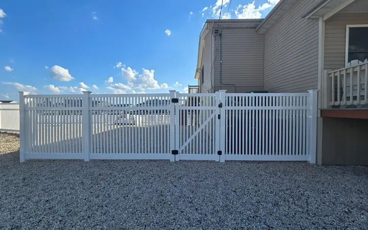 White vinyl fence with a walk gate on a gravel yard