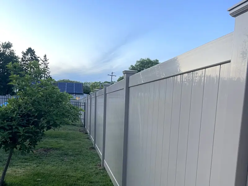 Tan vinyl privacy fence running along a lawn